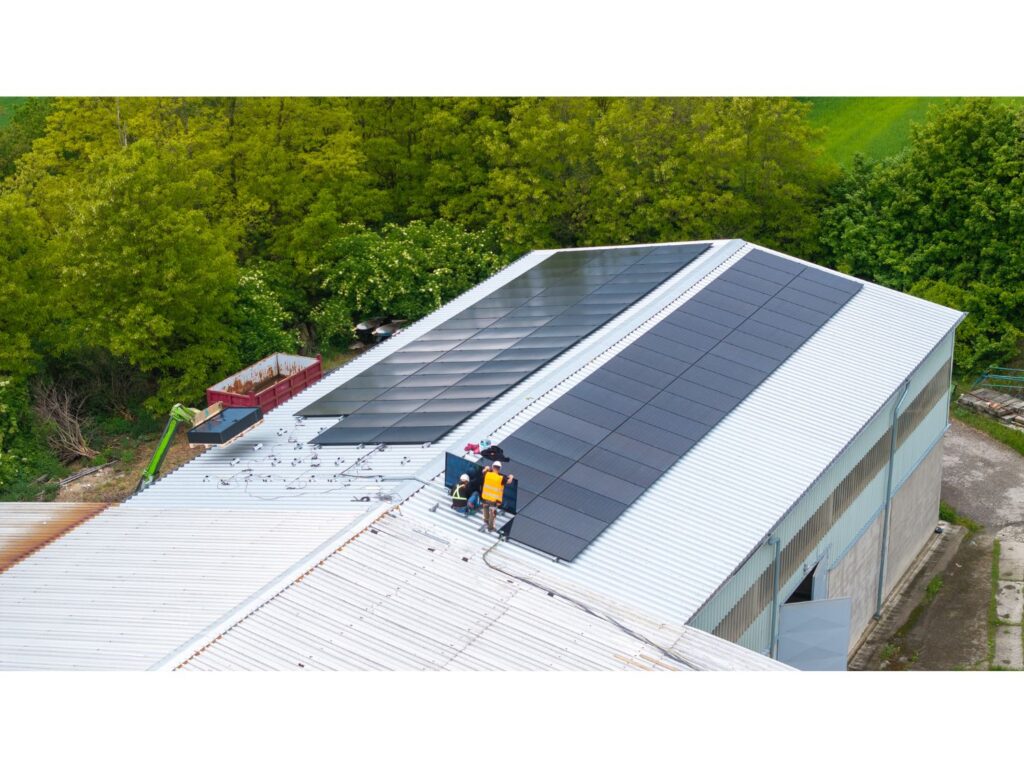 Pracovníci pokládají fotovoltaické panely na rozlehlou střechu haly.