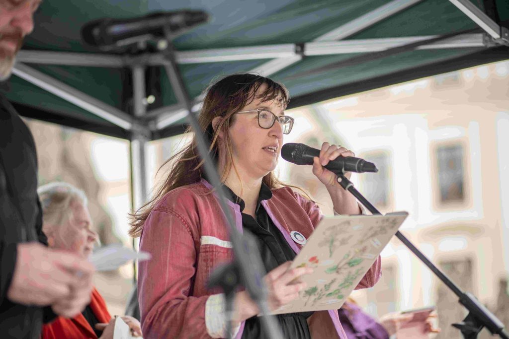 Žena mluvící na demonstraci do mikrofonu.