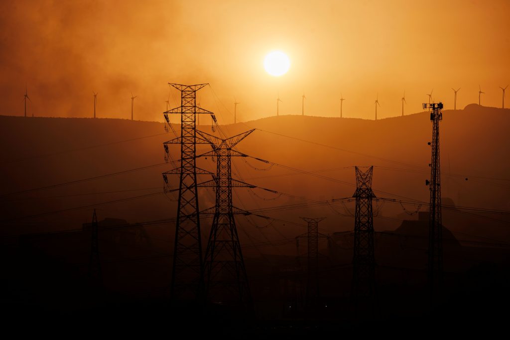Oranžovo černý záběr na energetickou infrastrukturu - vedení vysokého napětí a větrné turbíny v dálce.