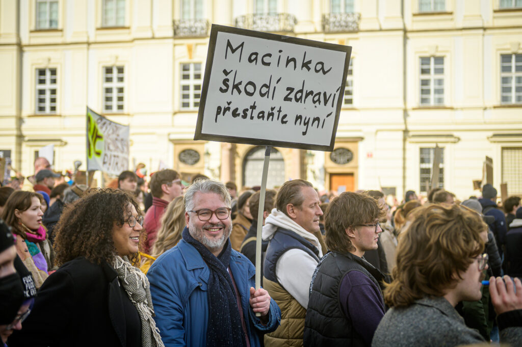 Demonstrace, člověk drží piket s nápisem Macinka škodí zdraví.