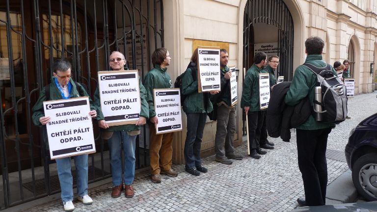 Skupina lidí drží protestní cedule před úředně vypadající budovou.