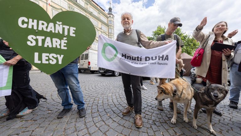 Skupina protestujících v Praze, člověk drží transparent Hnutí DUHA.